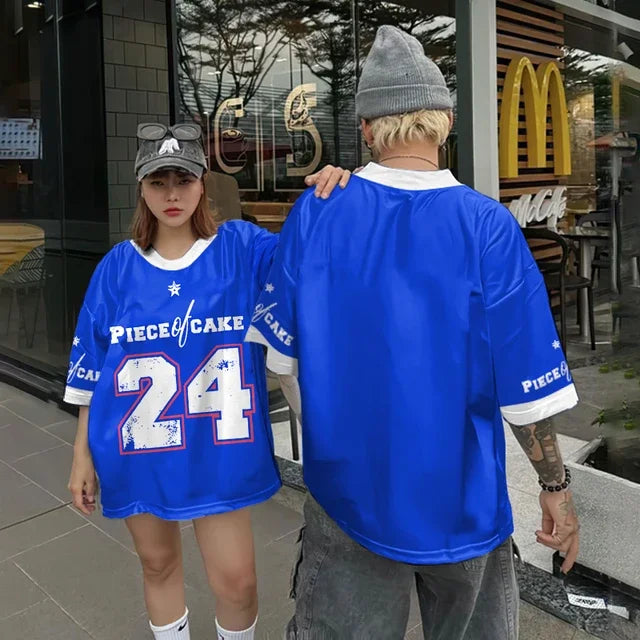 Two people model oversized blue short sleeve tops with white trim, star graphics, and a large number 24 design outside a cafe. Vivodeco casual streetwear