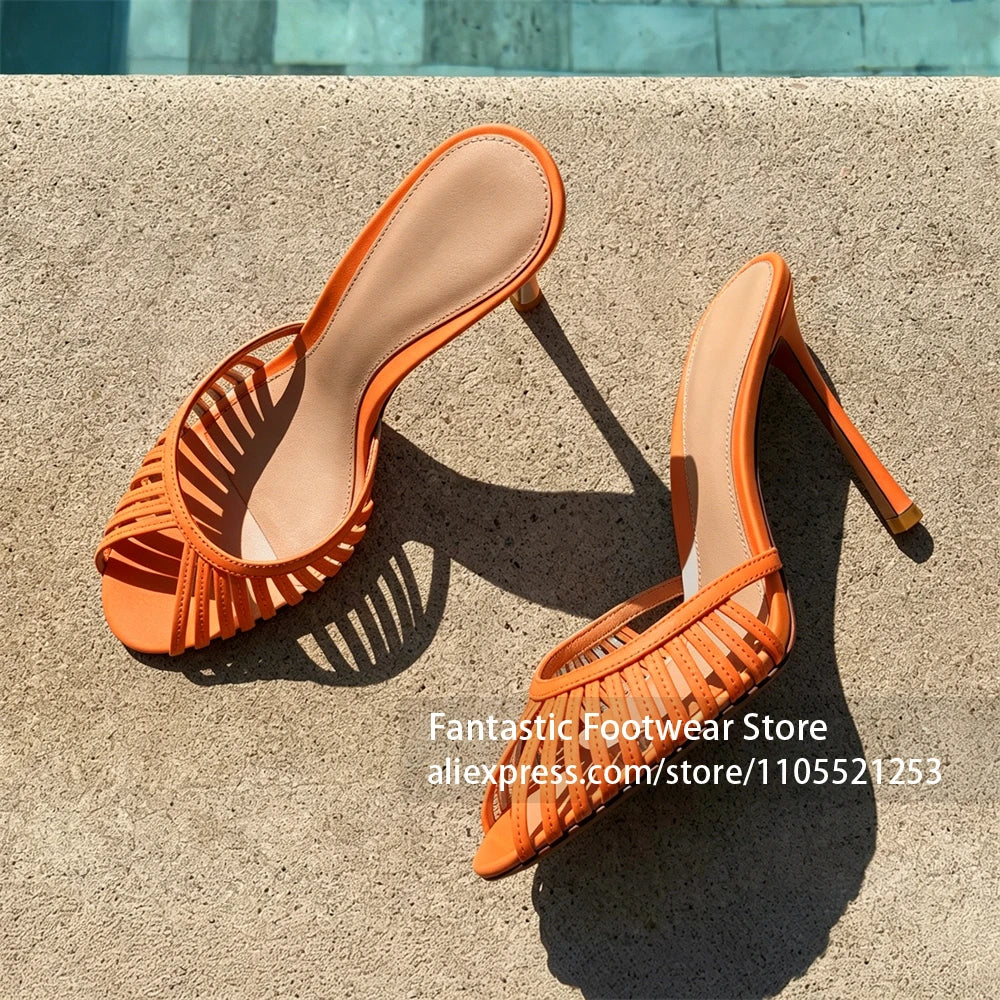 Vivodeco orange strappy sandals with slim high stiletto heels and open toes, displayed on a sunlit concrete surface with strong shadows.