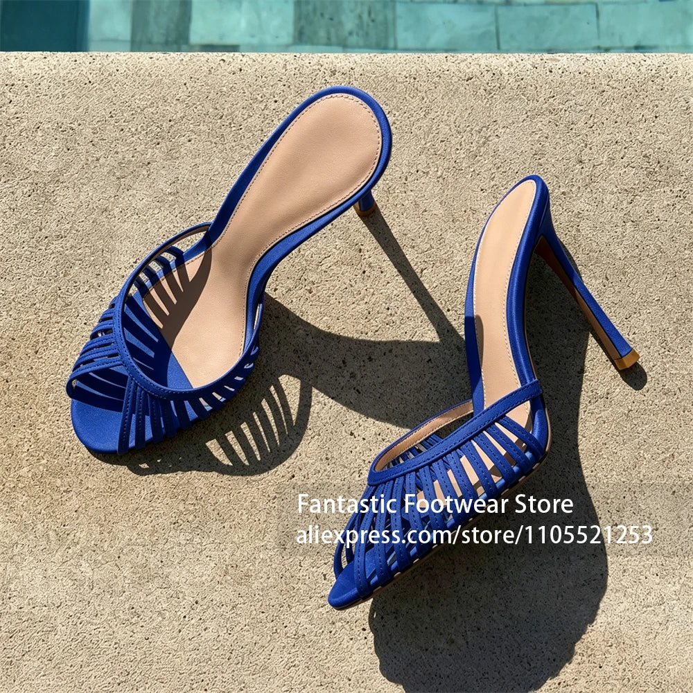 Pair of Vivodeco blue open toe mule sandals with narrow woven straps, beige insoles, and slim stiletto heels displayed on sunlit concrete.